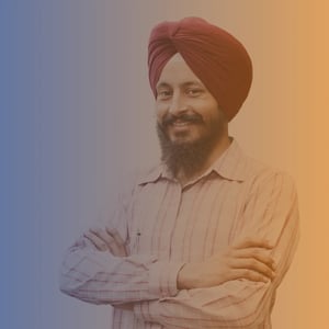 Early 40s Sikh man with arms crossed wearing a check white and pink shirt and maroon Dastar