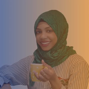 Late 20s smiling woman wearing a green headscarf, striped blouse and holding a mug of tea