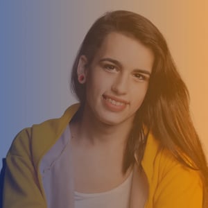 Mid 20s trans female with long hair wearing a yellow hoodie