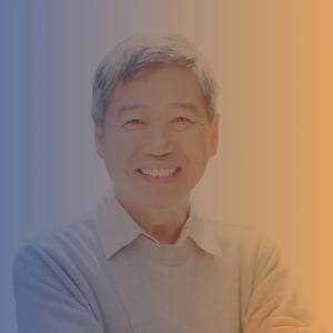 Mid 50s smiling Chinese man with short grey hair wearing a white shirt and grey sweater