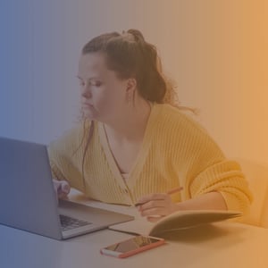 Young woman with Downs Syndrome working at a laptop wearing a yellow sweater